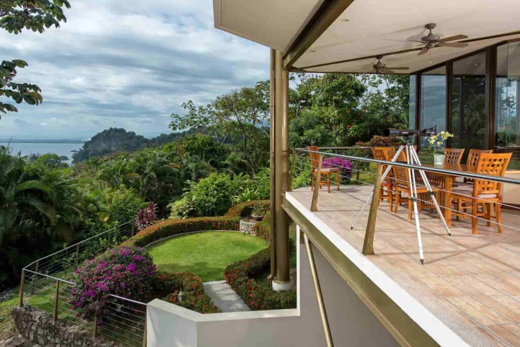 An outdoor patio in Costa Rica is surrounded by lush greenery with a wooden dining set sitting on the patio.