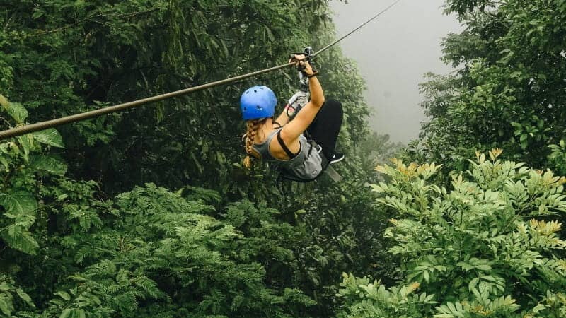 A woman in a blue helmet ziplining through a lush green rainforest in Costa Rica.