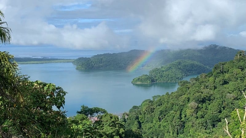 A rainbow stretching over a body of water surrounded by lush green trees in Costa Rica.
