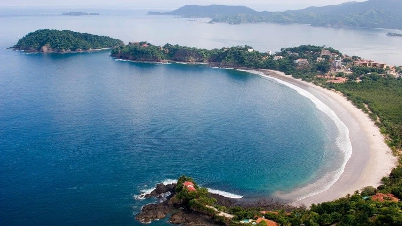 A beautiful bay with clear blue water surrounded by greenery and secluded homes in Costa Rica.