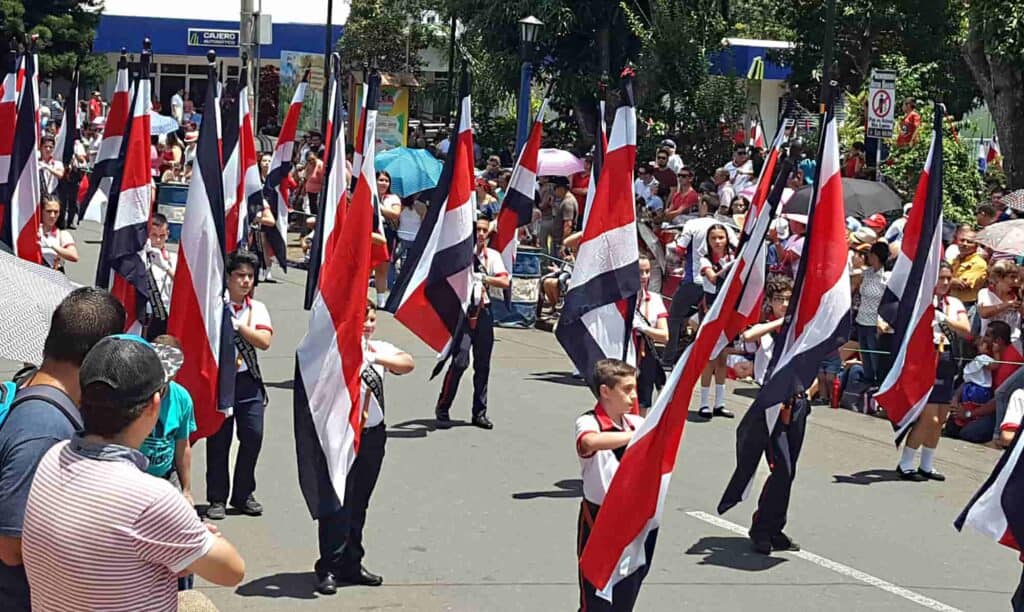 Several children walking down a street, each holding the Costa Rican flag during a parade.