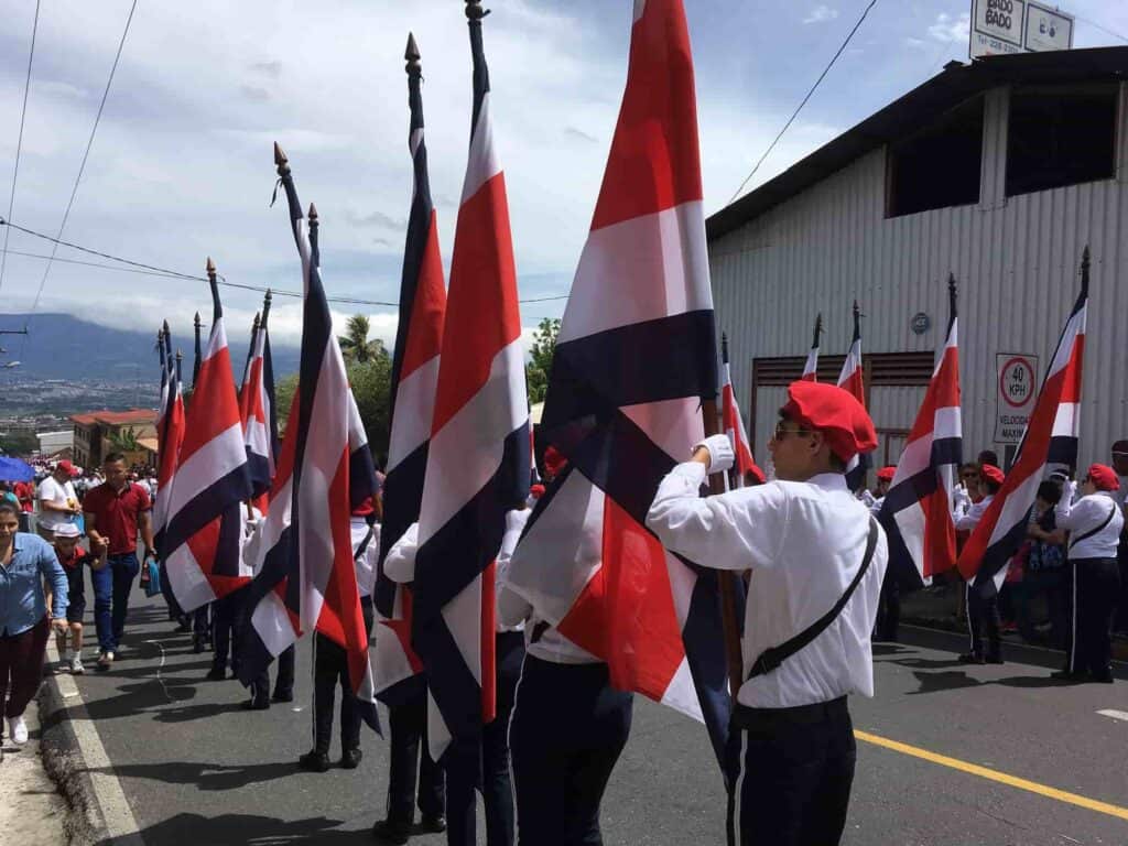 Several men wearing red berets and white shirts holding the Costa Rican flag in a line.