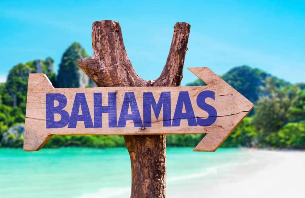 A wooden sign is attached to a stick that says "Bahamas" in purple letters and points to the right.