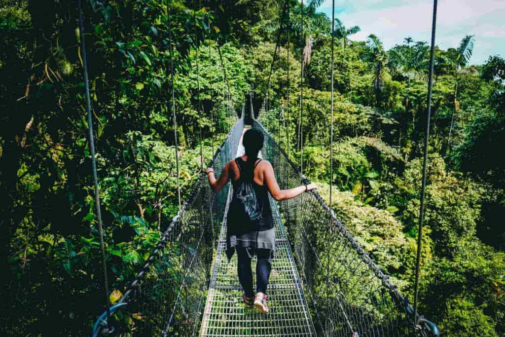 A woman wearing a backpack walking across a hanging bridge through the jungle in Costa Rica.