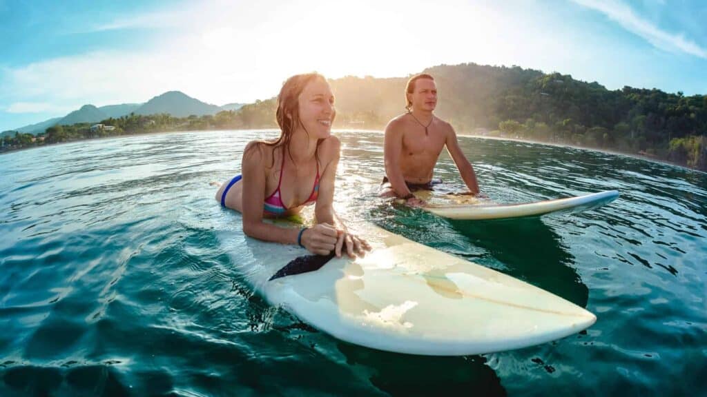 A woman and a man riding on surfboards in the ocean in Hawaii.