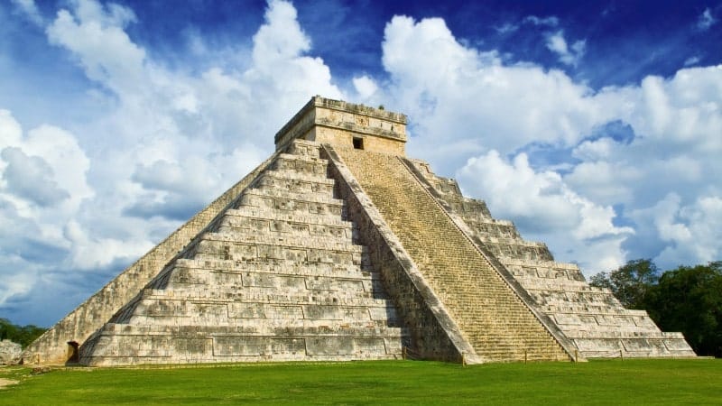 A famous Mayan pyramid sitting on a green lawn with a blue sky in the background in Mexico.