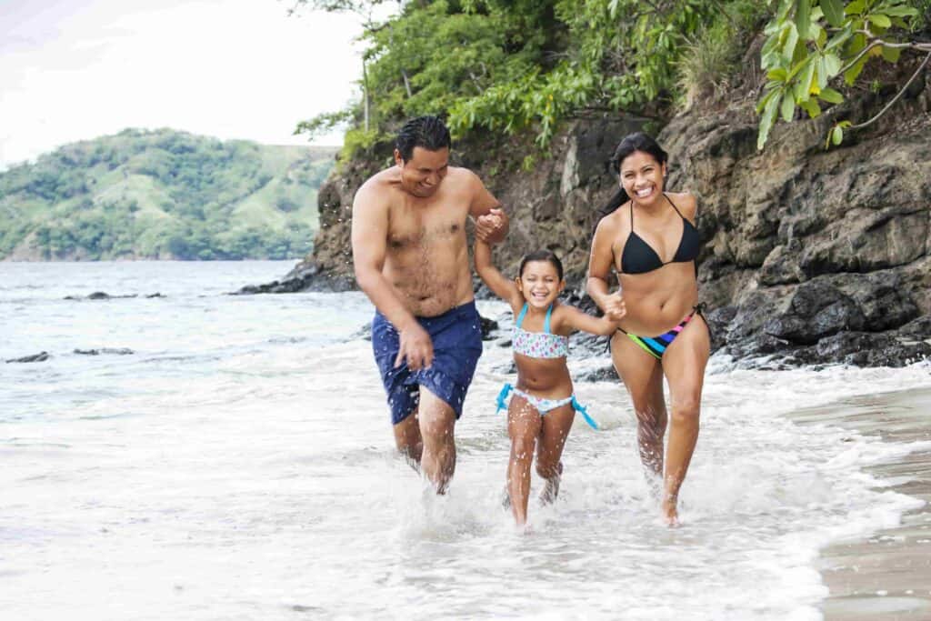 A family (dad, mom, and daughter) running through the waves in Costa Rica on the beach.