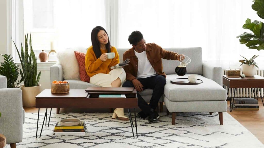 A couple sitting on a couch and pouring a cup of coffee into a mug.