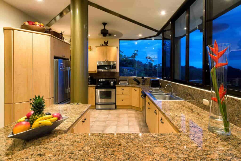 A kitchen in Costa Rica with granite countertops, a fruit bowl, and flowers sitting on the counter, as well as stainless steel appliances.