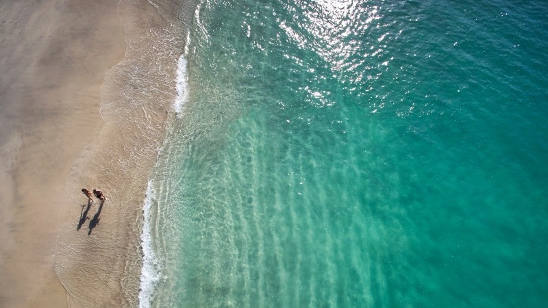 An aerial view of a turquoise beach in Costa Rica with two people walking by the ocean 