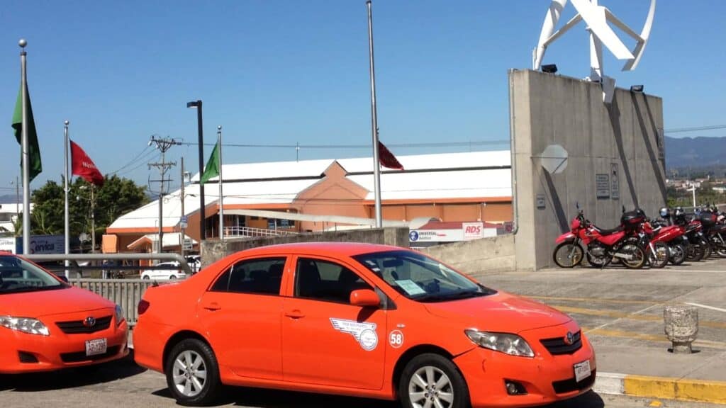Two orange cars sitting in front of a building and parking lot in Costa Rica.