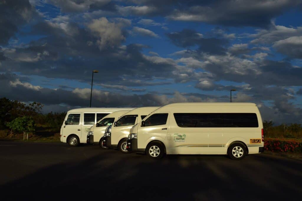 Four white shuttles are sitting on the pavement with an overcast sky.