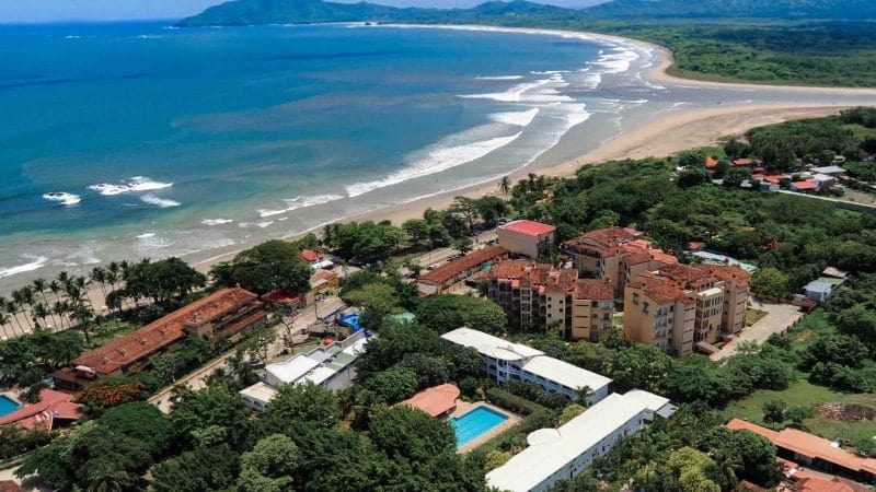 An aerial view of Playa Tamarindo and the town of Tamarindo, featuring orange and brown buildings and a pure blue ocean.