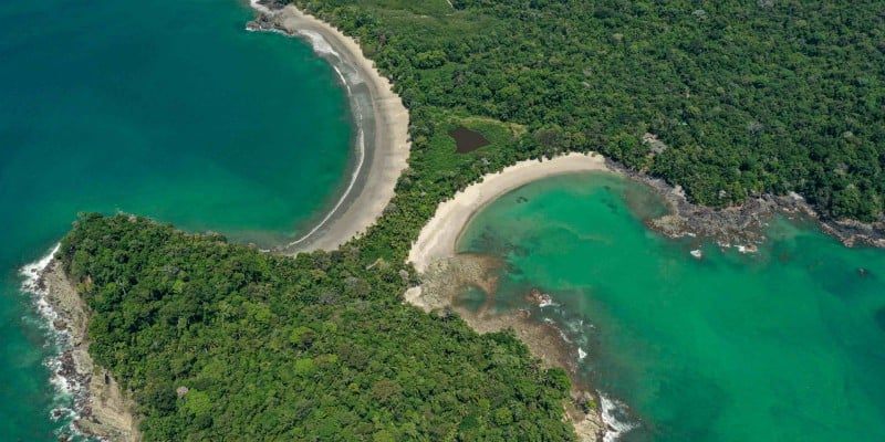The blueish green waters and lush greenery of Manuel Antonio National Park from an aerial view.