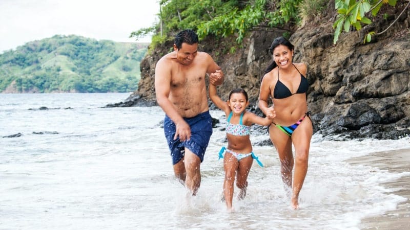A family with a dad, mom, and young daughter running through the ocean in Costa Rica.