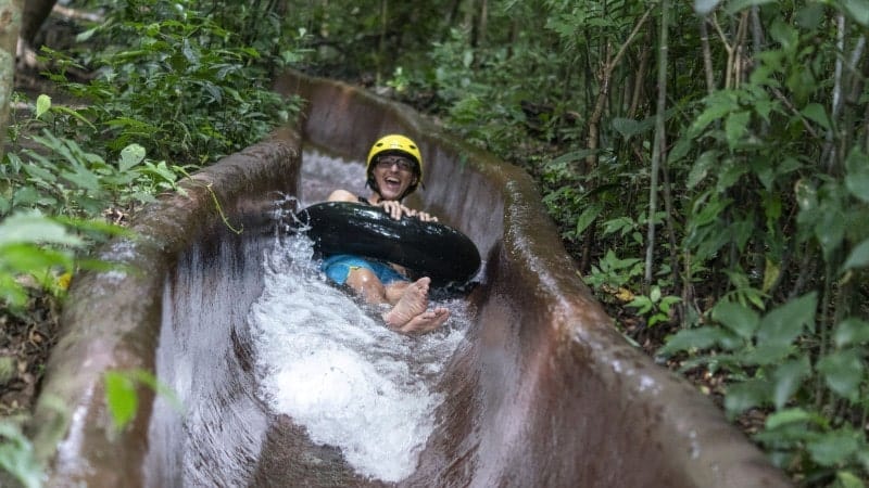 A kid wearing a yellow helmet sliding down a waterslide in a black tube.