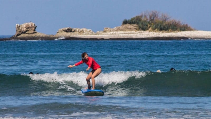 A woman in a red long-sleeve surf shirt surfing in Playa Tamarindo.