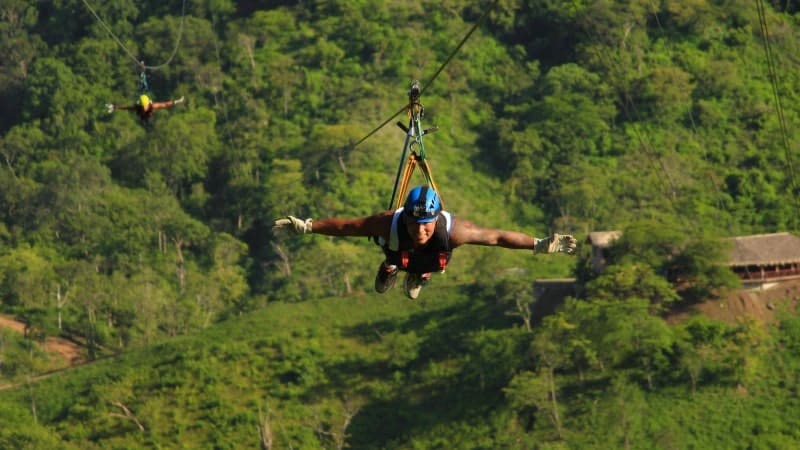 A man ziplining over a lush green rainforest and wearing a blue helmet