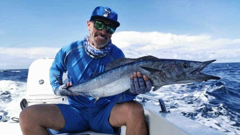 A man holding a wahoo fish on a boat on the ocean