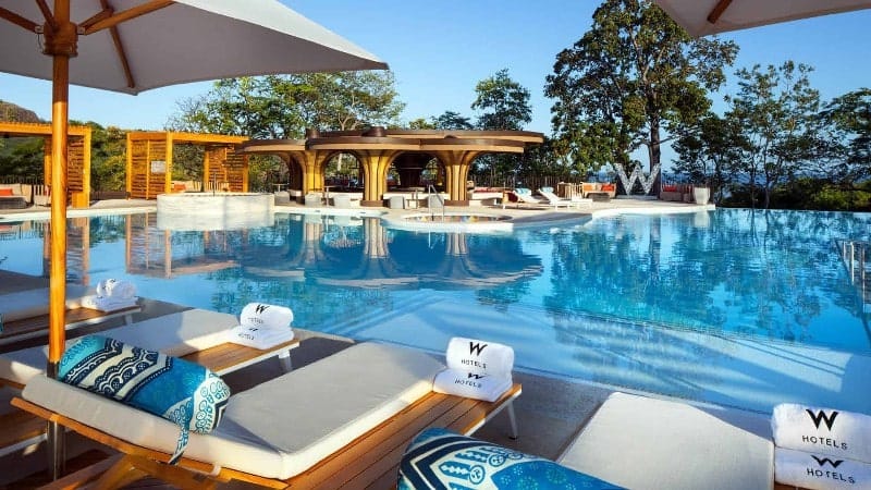 The beautiful pool at the W Costa Rica Resort Hotel, featuring luxurious towels, pillows and a integrated food and drink table at every lounger, plus a swim up bar, private cabanas and a view of the Pacific Ocean.