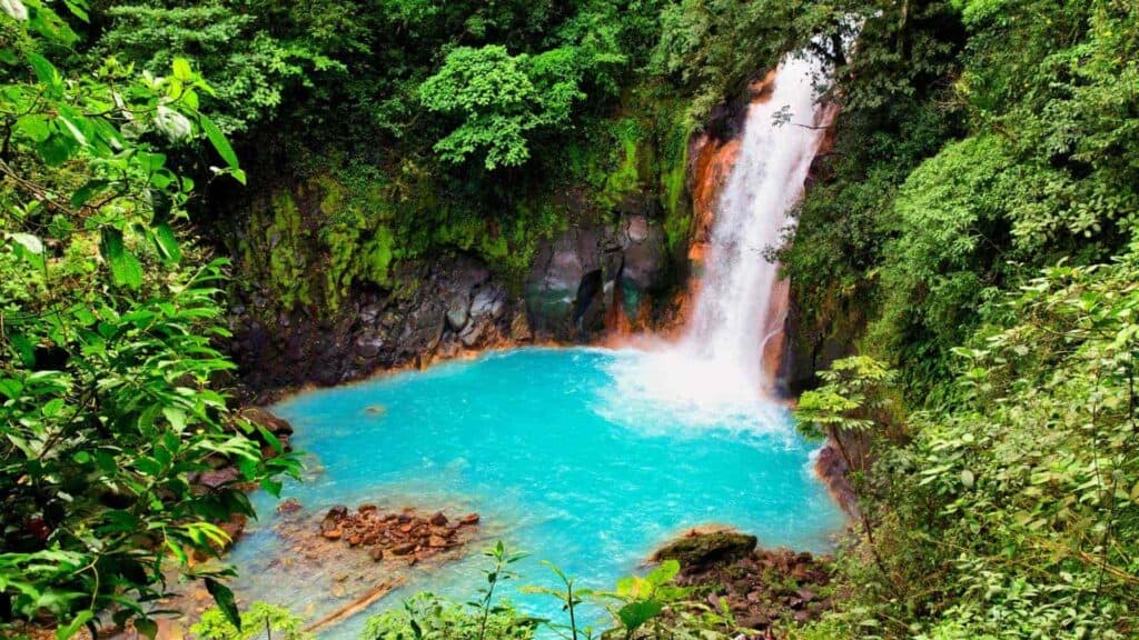 Waterfall going into turquoise water in Costa Rica. The waterfall is surrounded by green trees.