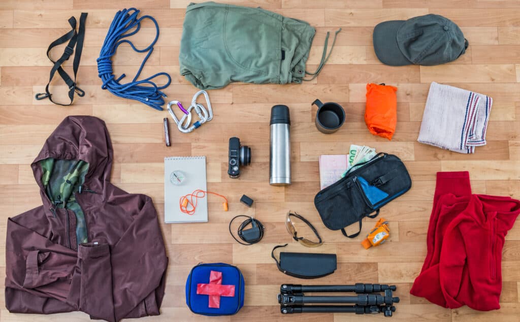 items you should pack with you on a wildlife adventure in Costa Rica. The image shows the following: ropes, pants, hat, clips, towel, mug, thermos, camera, charger, sunglasses, money, jacket, tripod, emergency kit, compass.