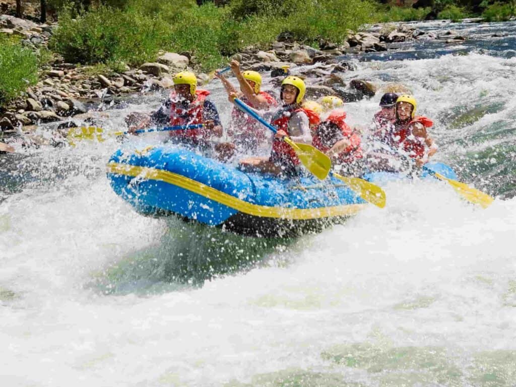 a group of people in a blue raft with a yellow strips going whitewater rafting