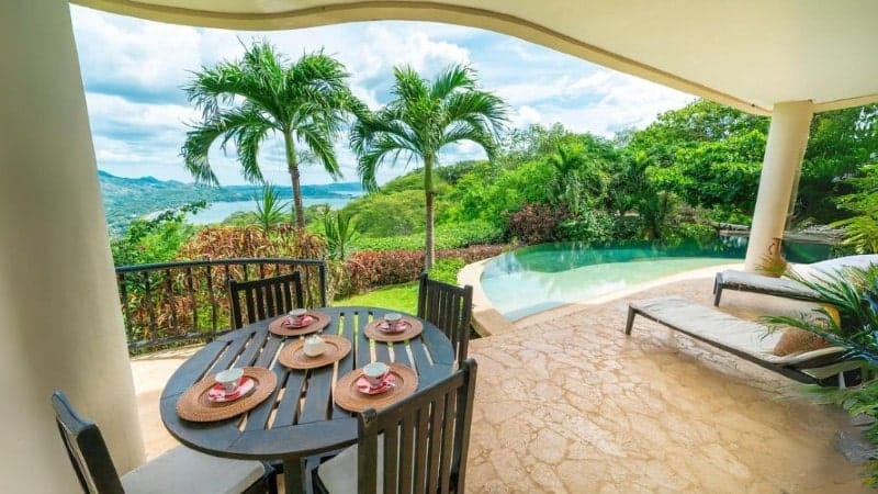 backyard of a vacation rental in Costa Rica with a table, lounge chairs, and a pool overlooking a beautiful view of green trees and the ocean in the background.