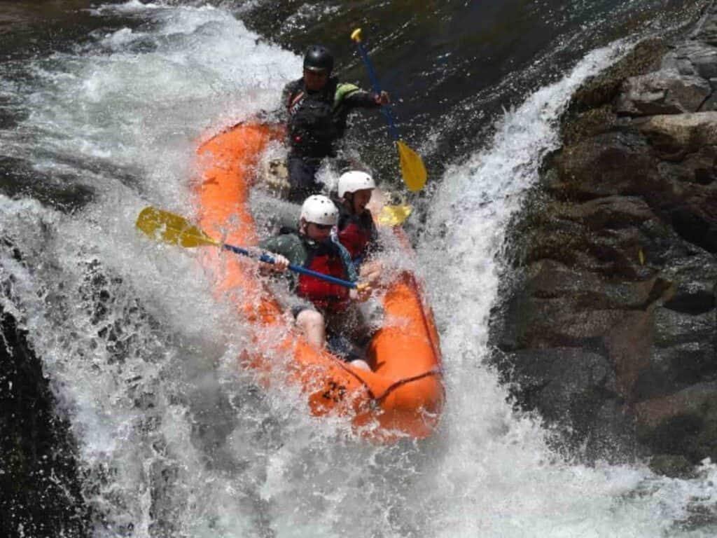 Three people white water rafting down the Corobici River in an orange raft and yellow oars in Costa Rica