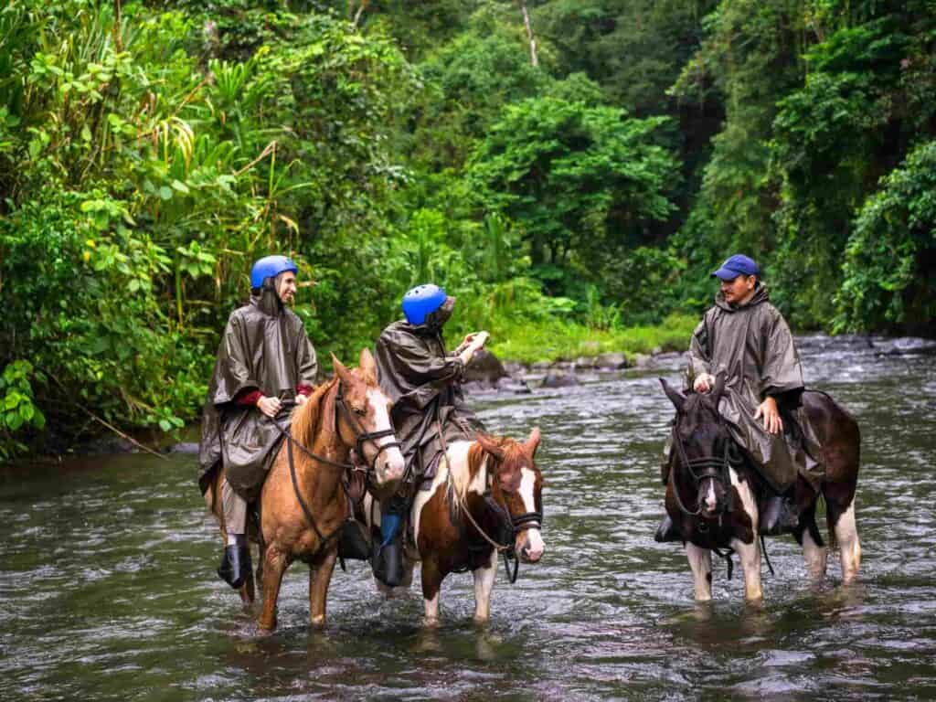 Three people horseback riding on three different horses while crossing a river