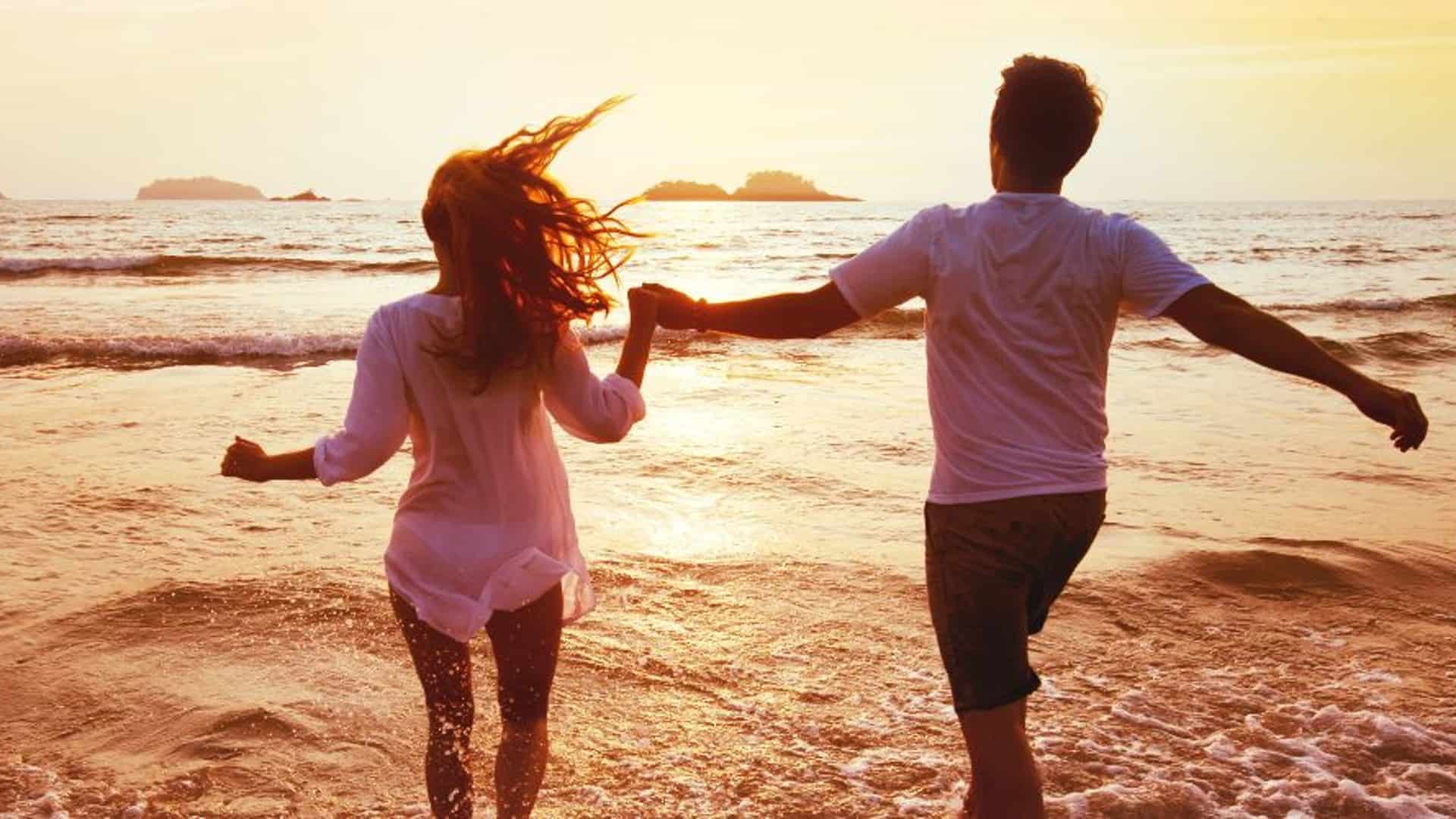 A couple joyfully runs along the beach at sunset.