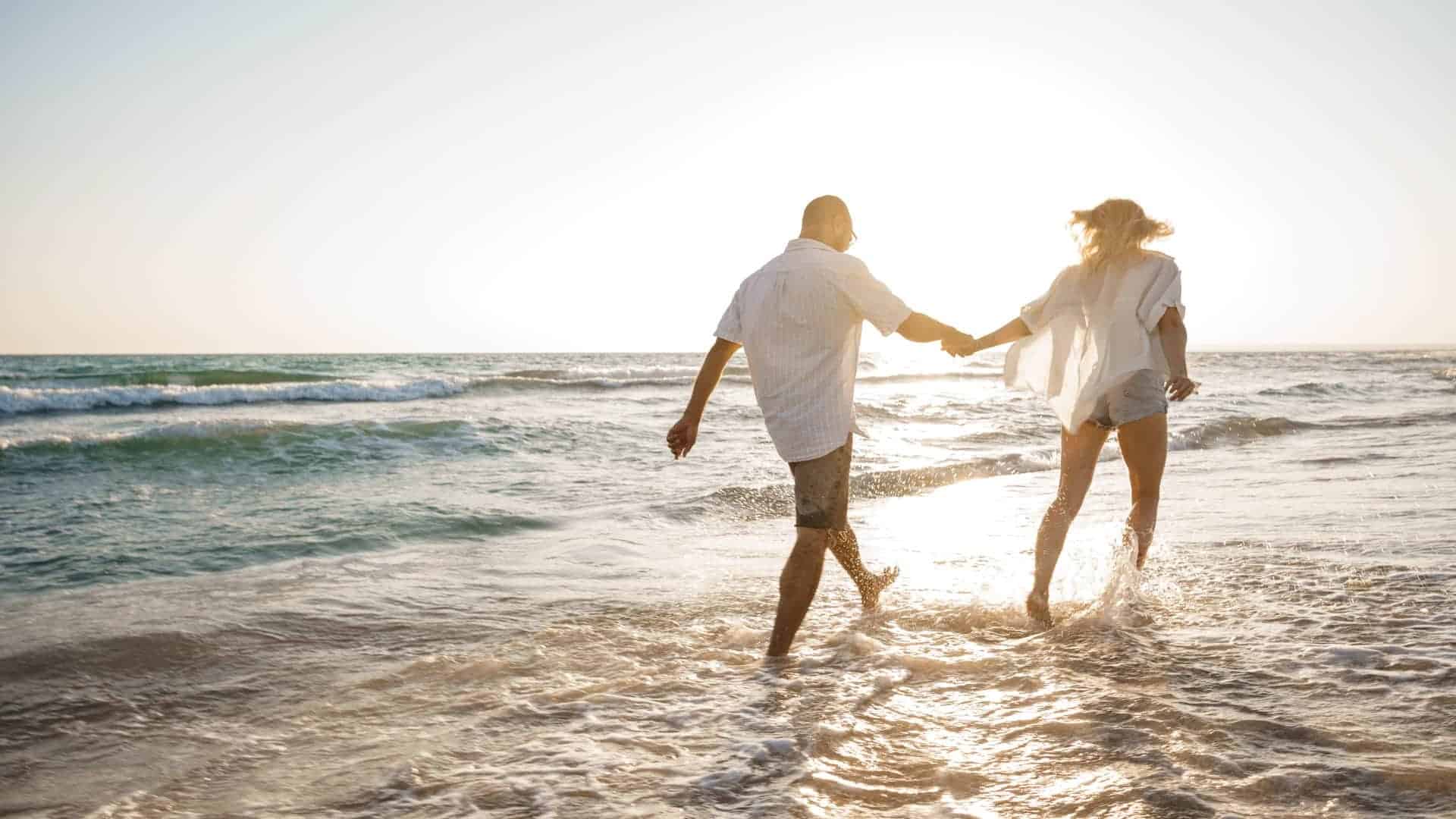 A man and woman are holding hands while walking on the beach.