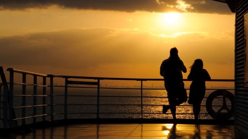 A silhouetted man and woman watching the sunset at sea.