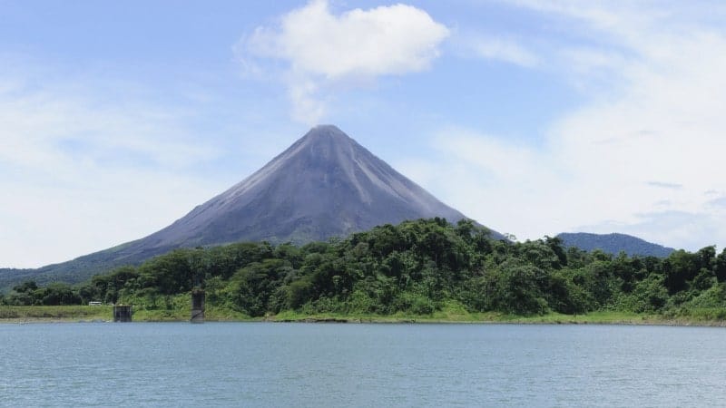 A volcano towering over the water with a forest of trees below it.