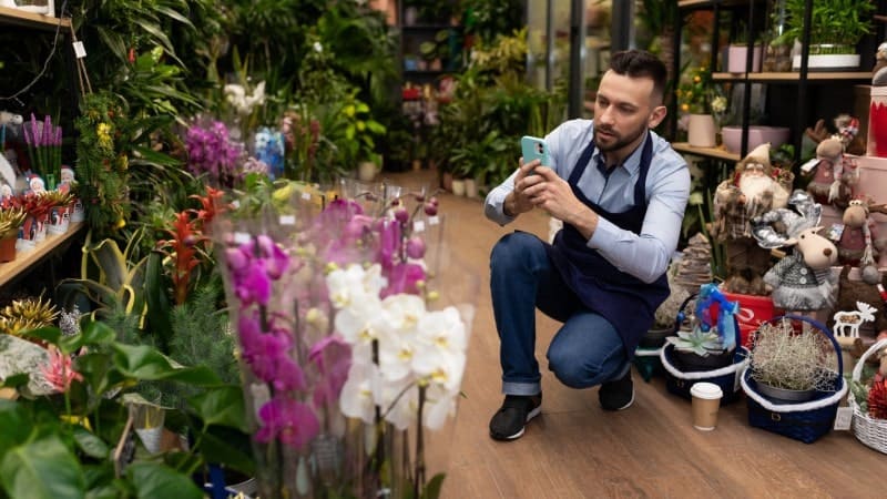 A man crouching down to take photos of orchids in a store.