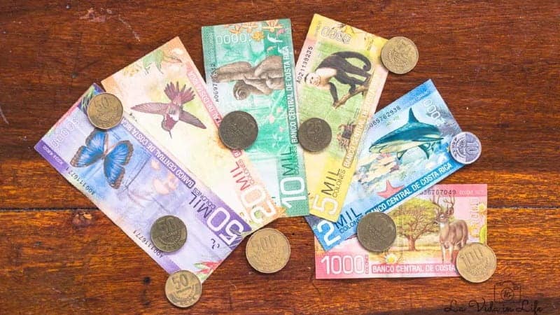 Various Costa Rican banknotes and coins are spread out on a wooden surface.