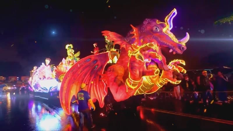 A vibrant night parade featuring a large, illuminated dragon float. The dragon is adorned with bright orange and red lights, emphasizing its intricate design and creating a fiery effect. 